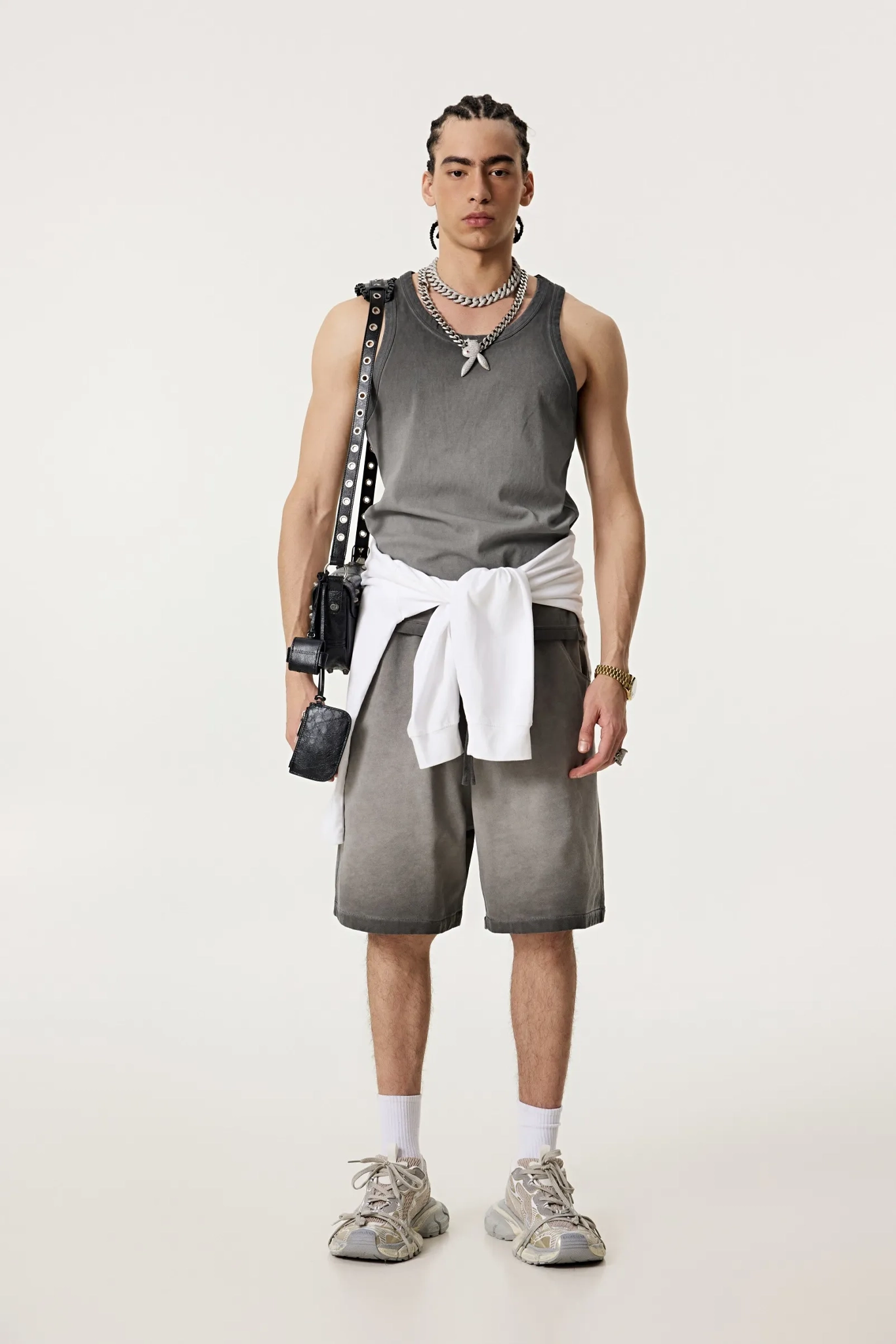 Person wearing a gray tank top and shorts with a white towel, standing against a plain background.