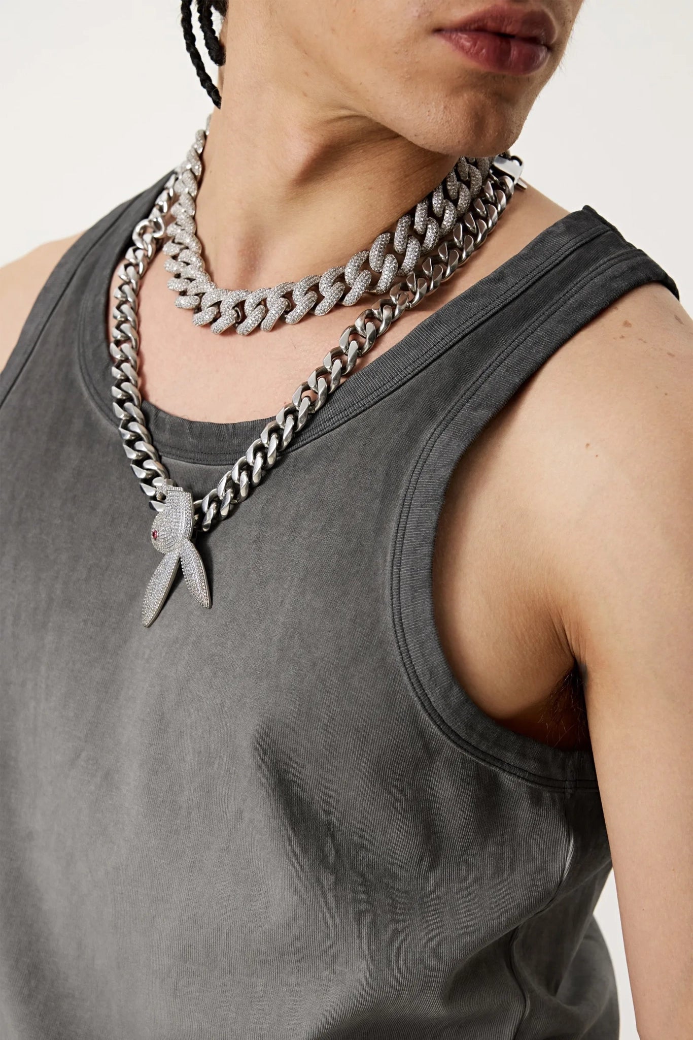 Person wearing a gray tank top and multiple chain necklaces with a white background