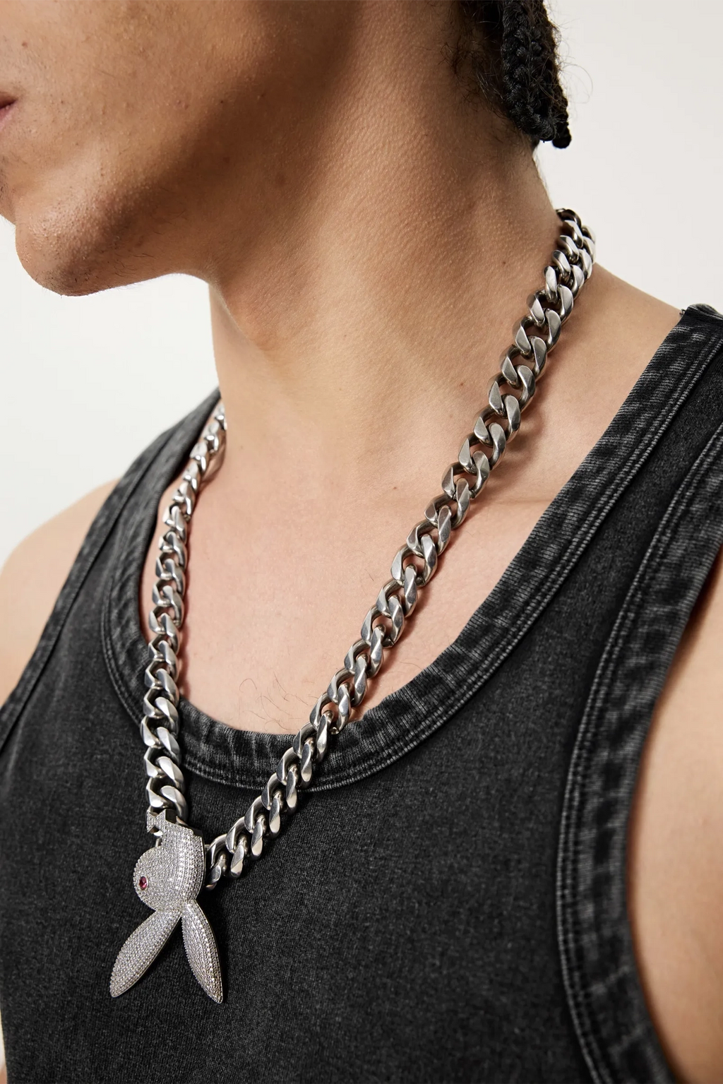 Person wearing a chain necklace with a pendant on a plain background