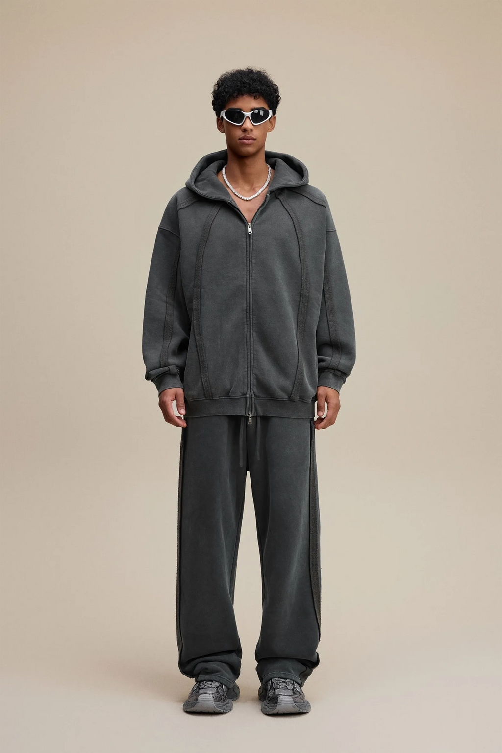 Person wearing a gray hoodie and pants on a beige background