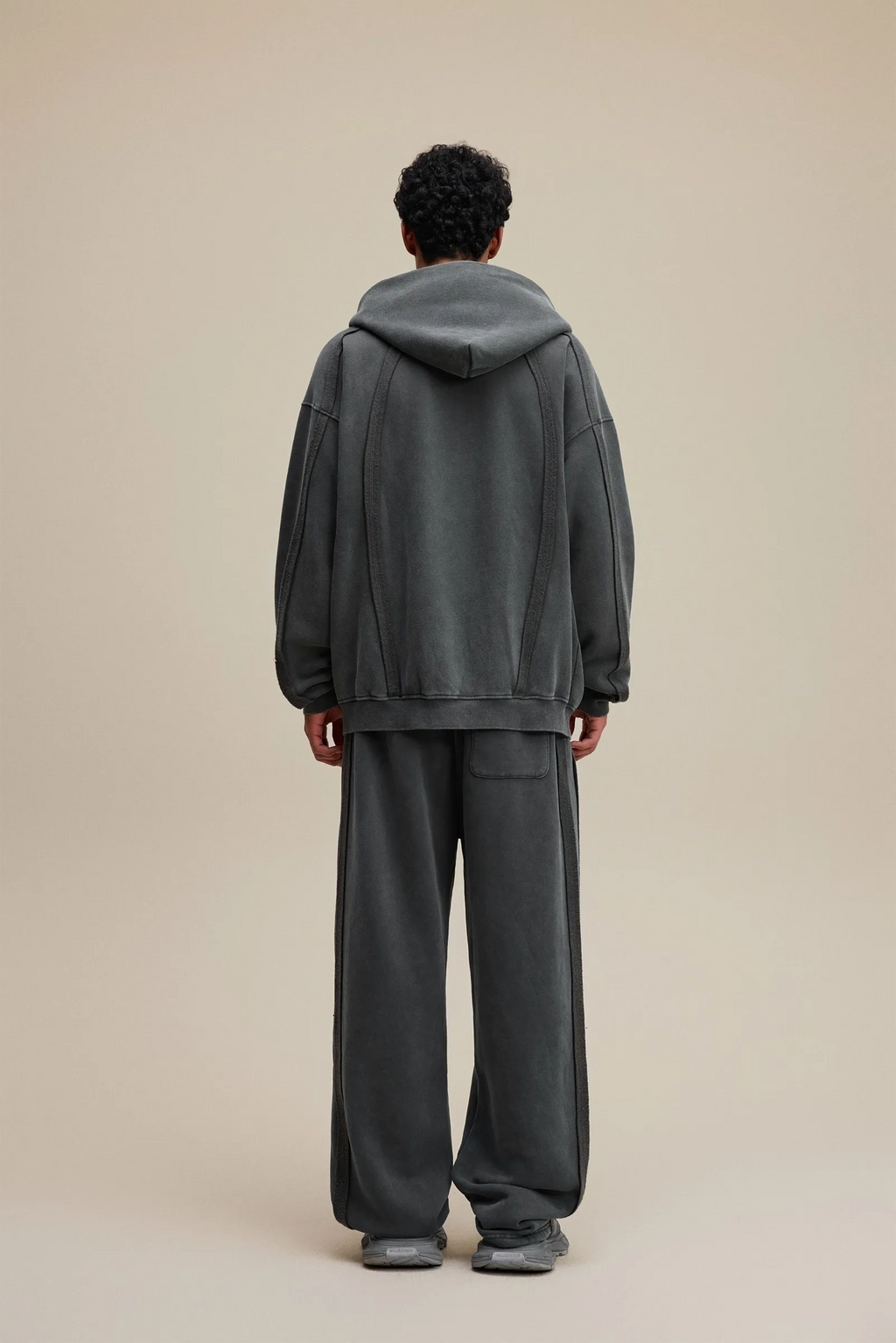 Person wearing a gray tracksuit standing against a beige background