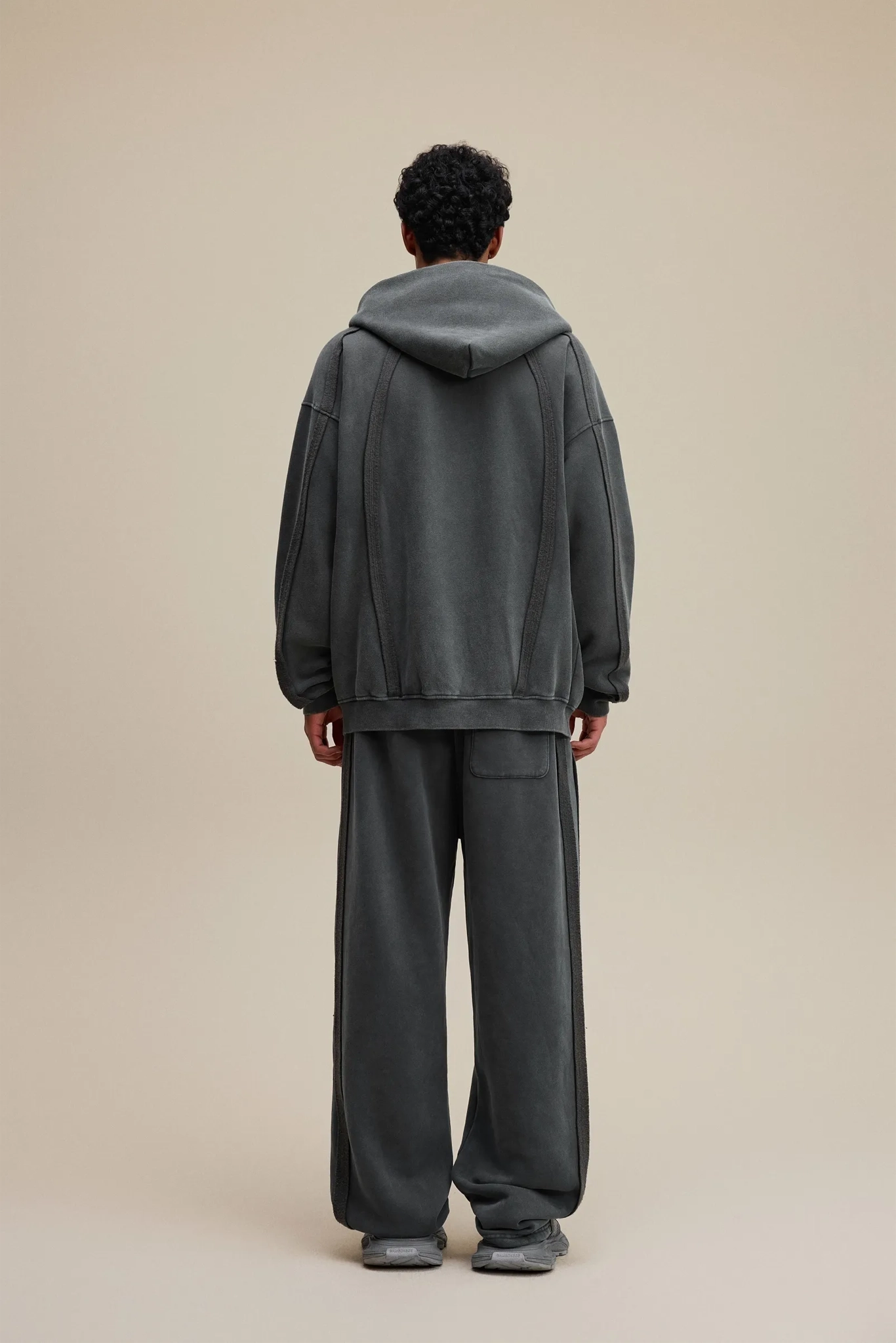 Person wearing a gray tracksuit standing against a beige background