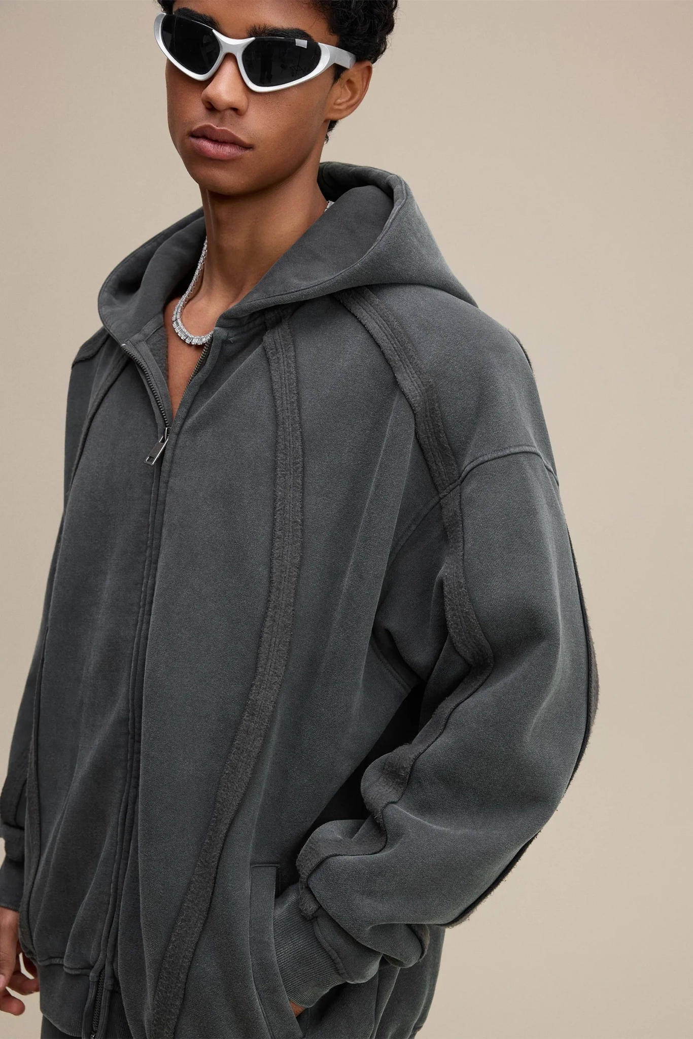 Person wearing a gray hoodie and sunglasses on a beige background