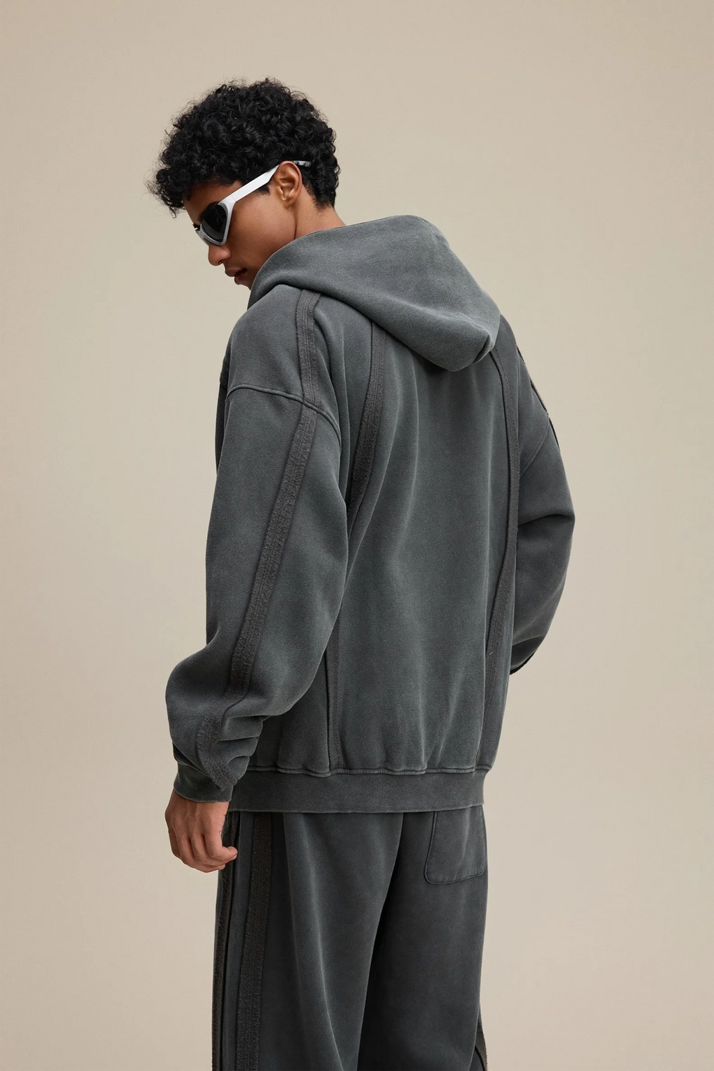 Person wearing a gray hoodie and pants on a beige background