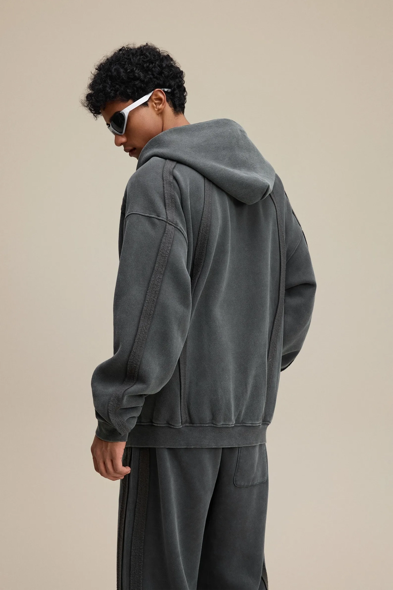 Person wearing a gray hoodie and pants on a beige background