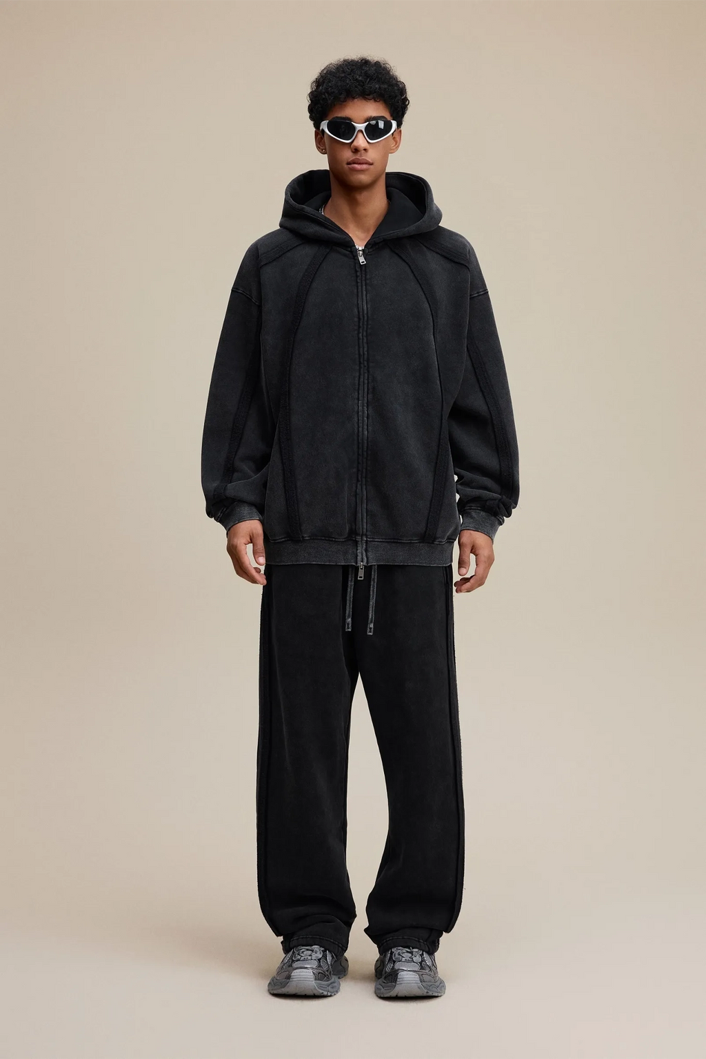 Person wearing a black hoodie and pants on a beige background