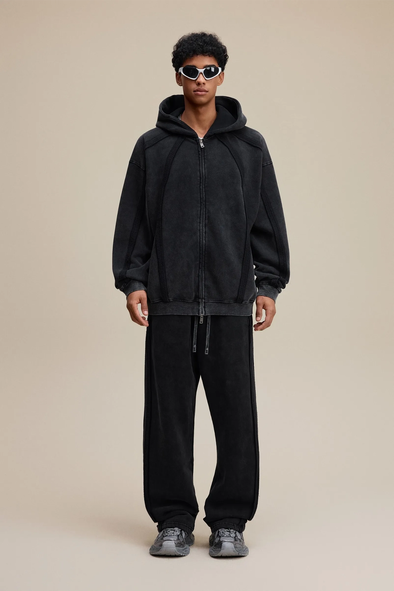 Person wearing a black hoodie and pants on a beige background