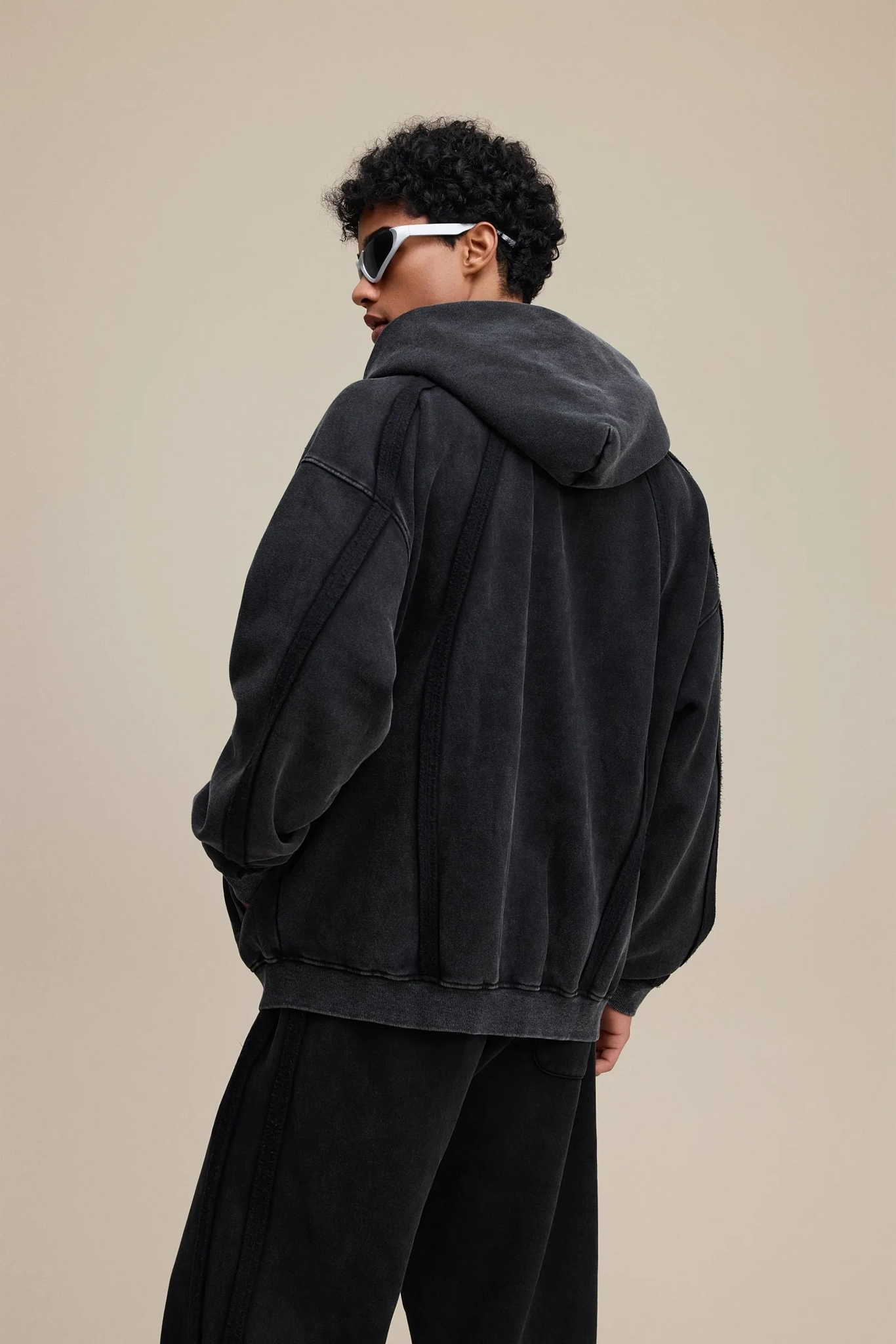 Person wearing a dark gray hoodie and sunglasses on a beige background