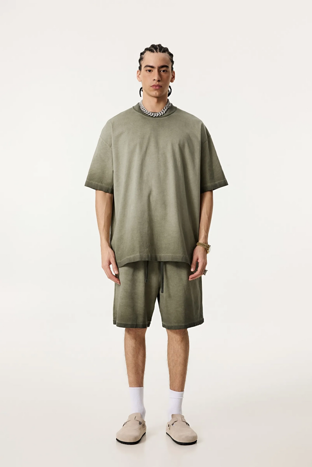 Person wearing an oversized olive green t-shirt and shorts set on a white background