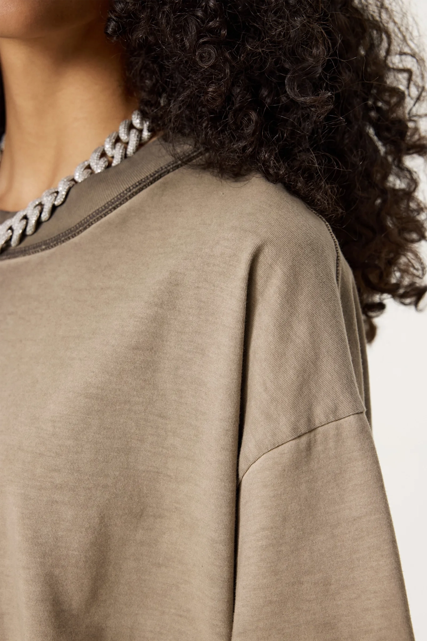 Close-up of a person wearing a beige long-sleeve top with a chain detail on a white background