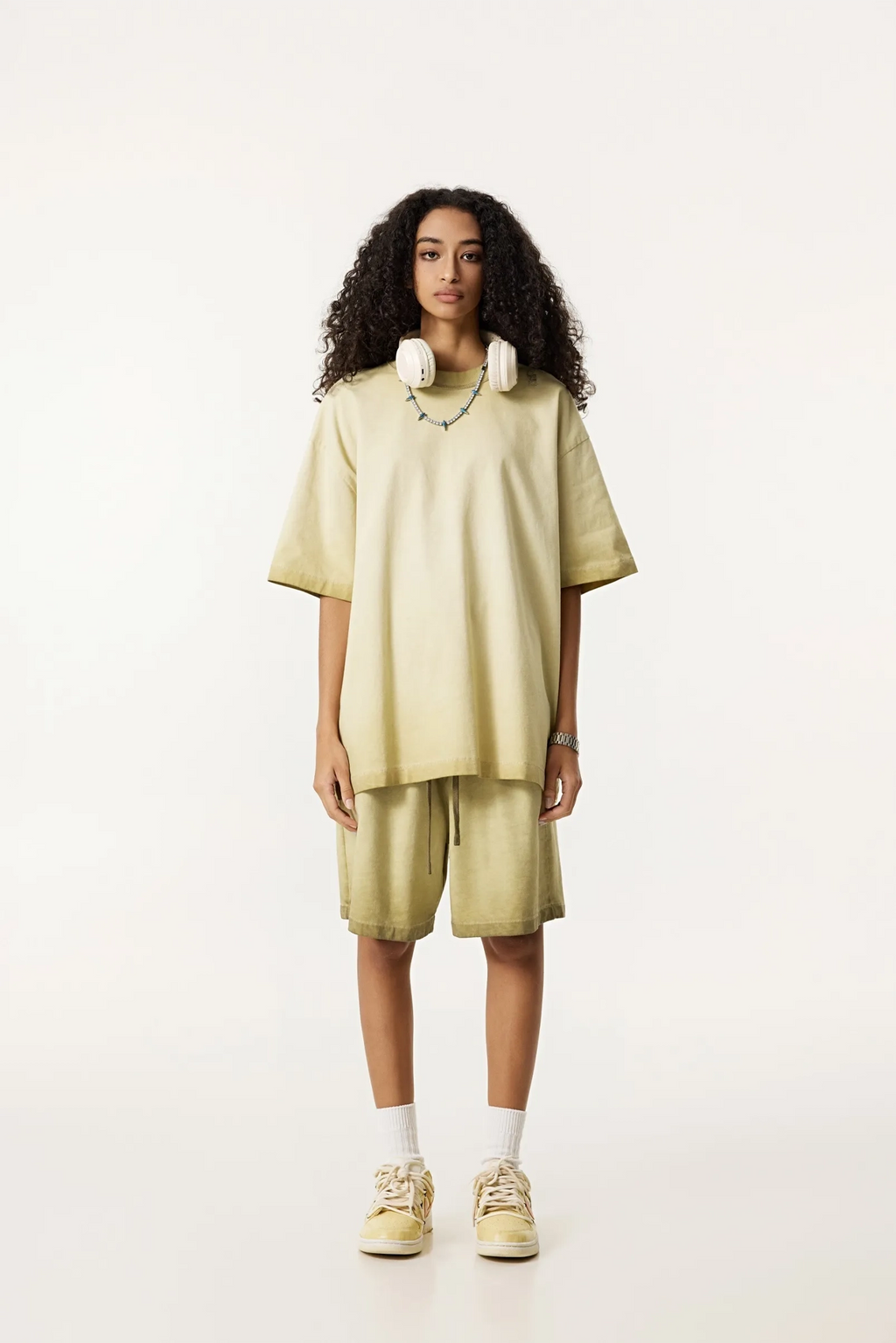 Person wearing a light green oversized t-shirt and shorts set on a white background