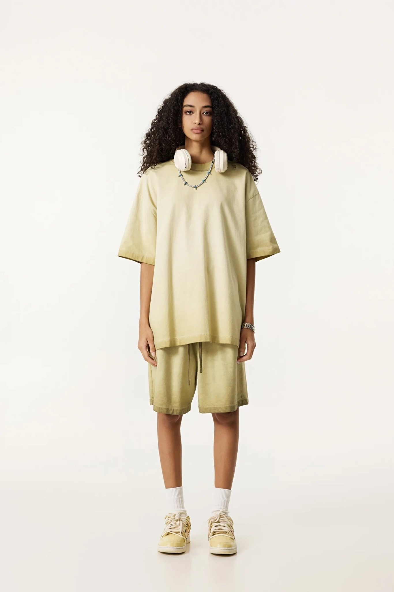 Person wearing a light green oversized t-shirt and shorts set on a white background