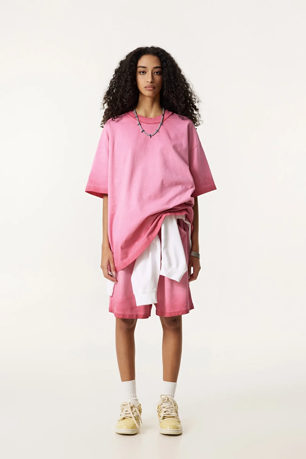 Person wearing a pink oversized t-shirt and shorts with white socks and shoes on a white background