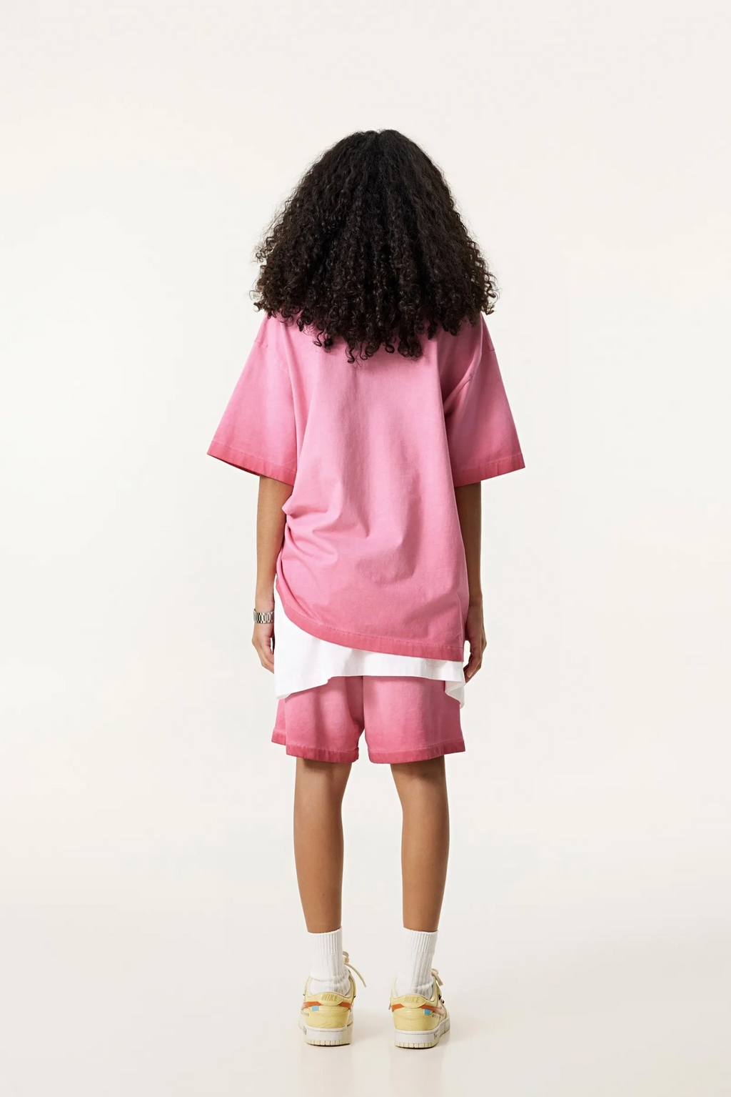 Person wearing a pink oversized shirt and shorts set on a white background