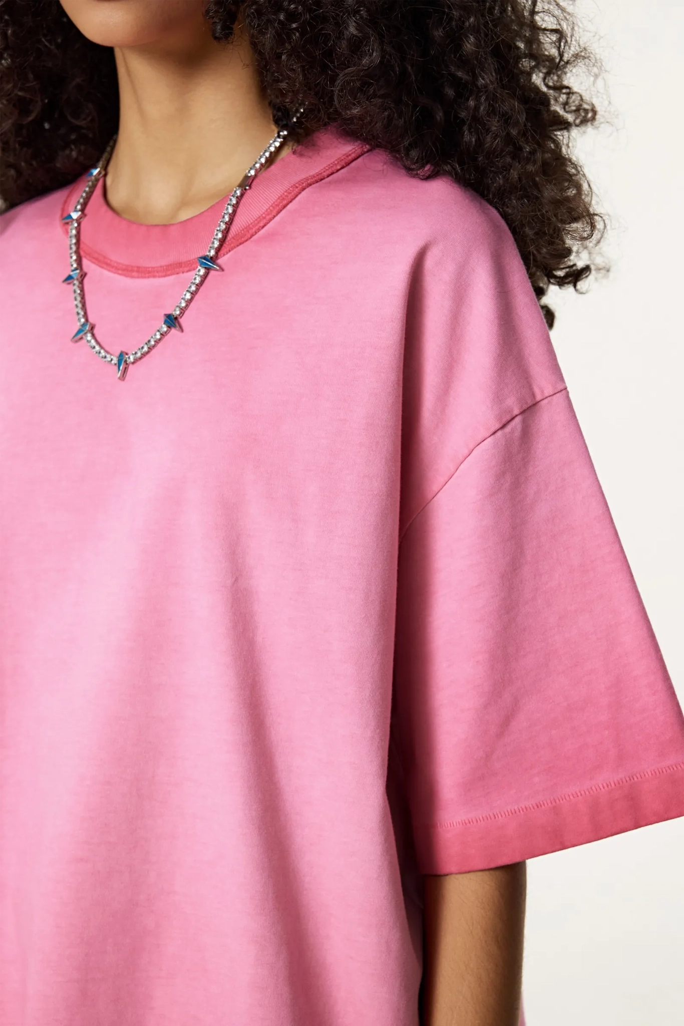 Person wearing a pink oversized shirt with a necklace on a white background