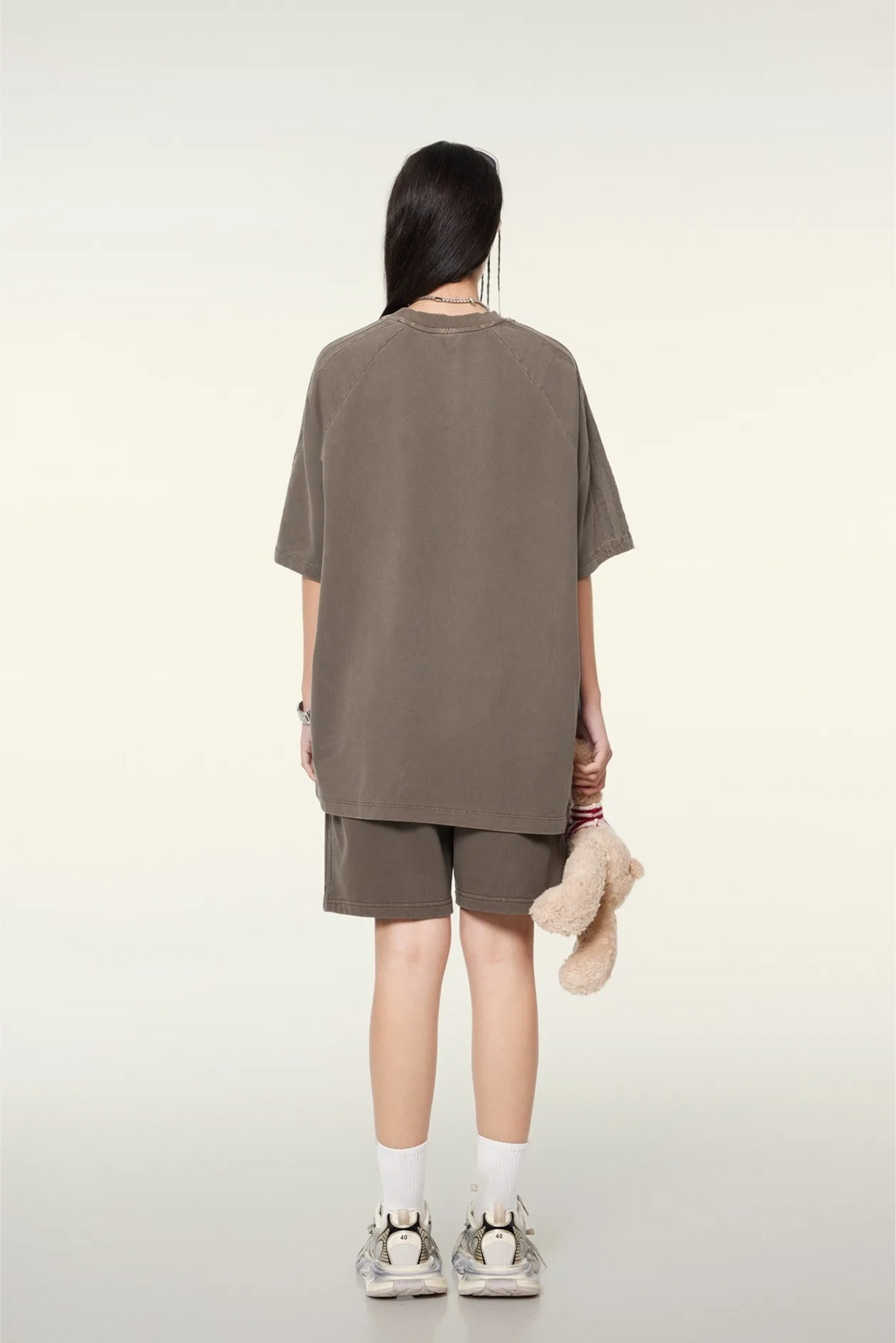 Person wearing a brown oversized t-shirt and shorts set on a white background