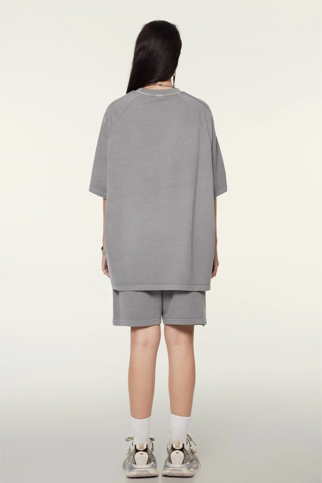 Person wearing a gray oversized t-shirt and shorts set on a white background
