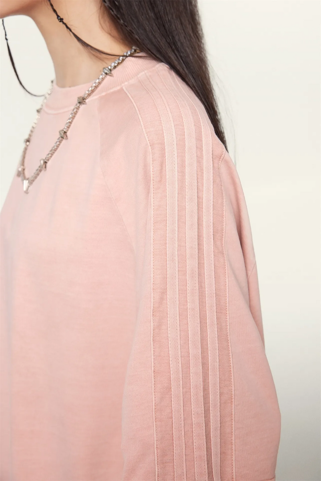 Close-up of a person wearing a light pink pleated garment with a blurred background