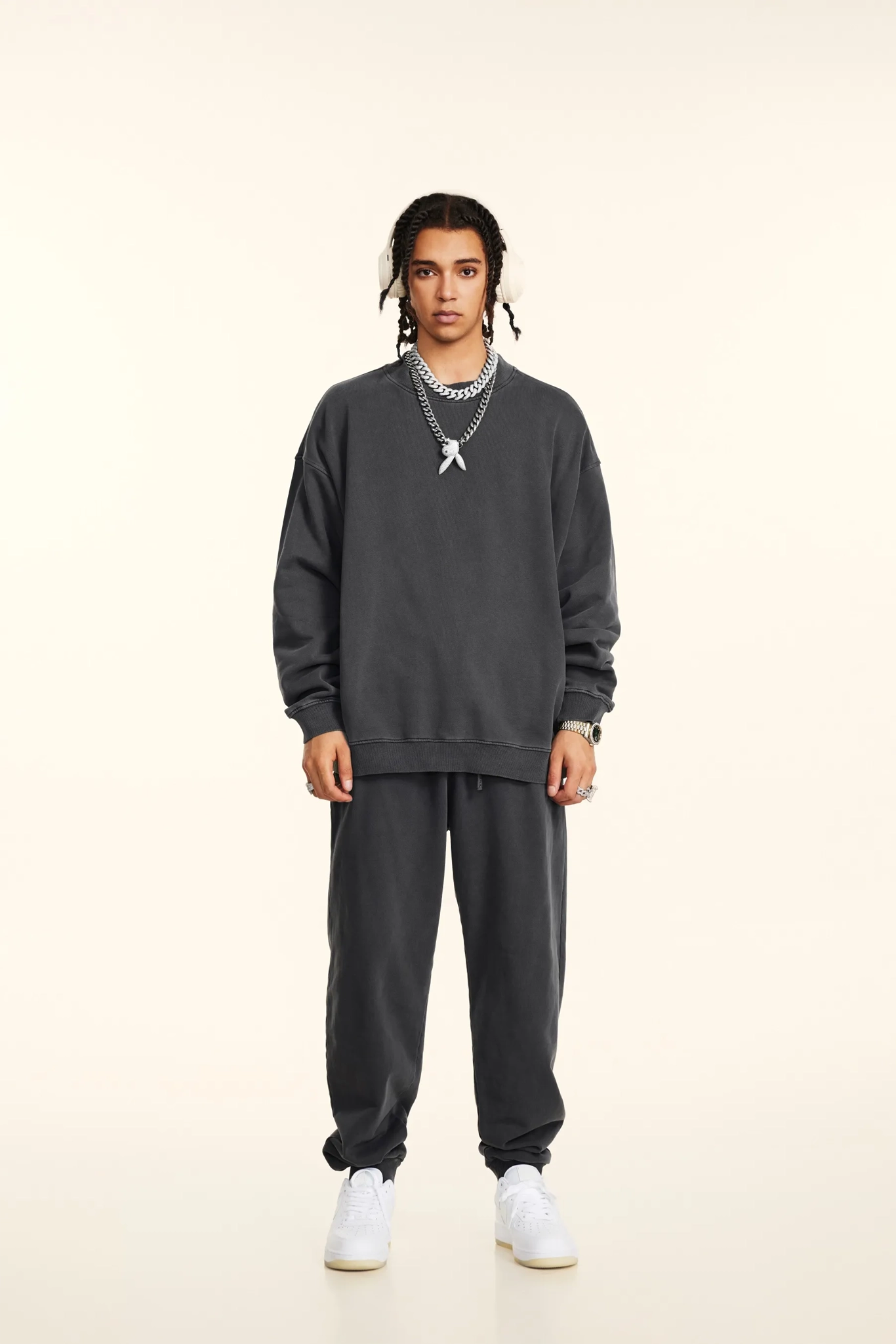 Person wearing a dark gray sweatshirt and pants with white sneakers on a beige background