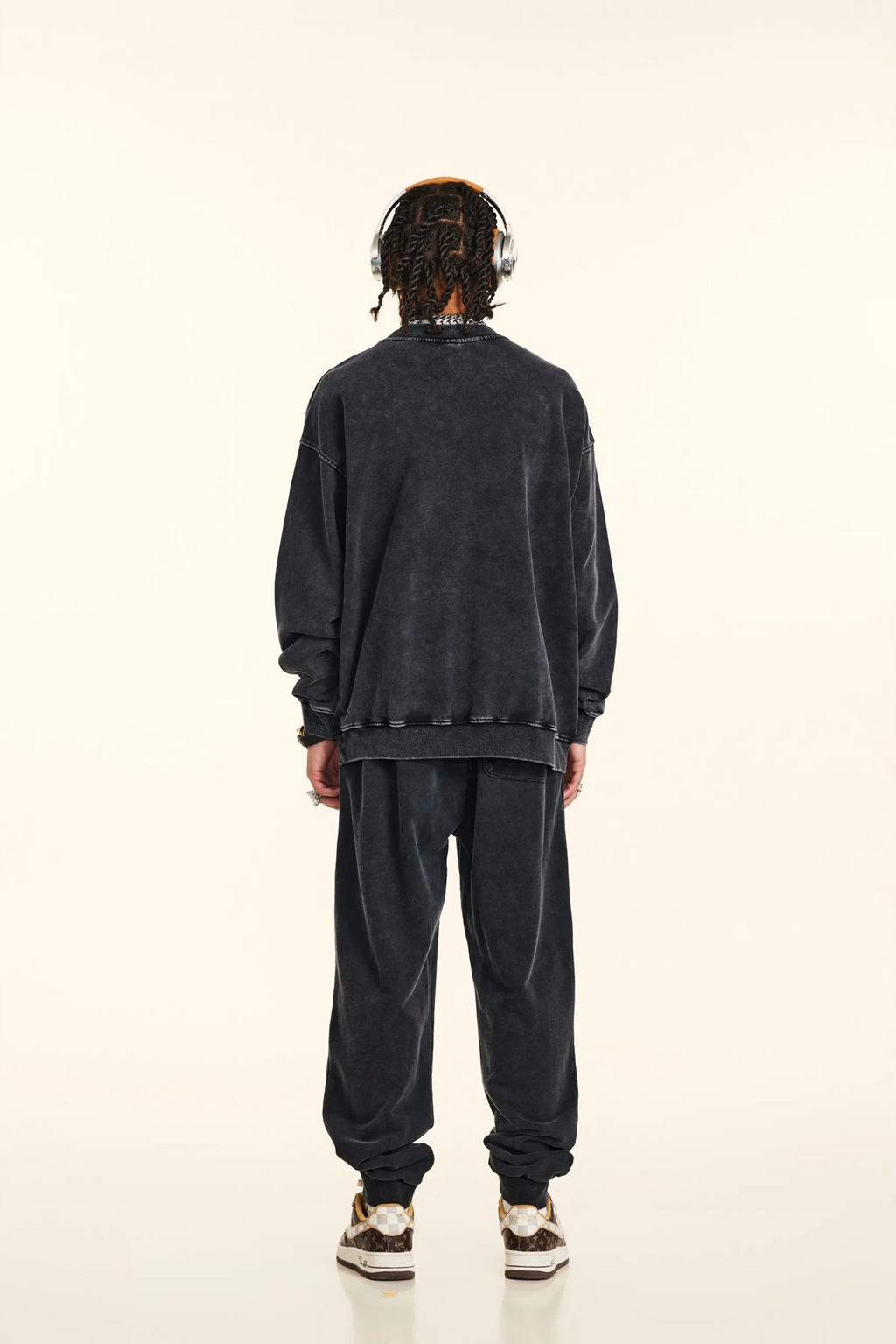 Person wearing a dark gray sweatshirt and pants with headphones on a white background