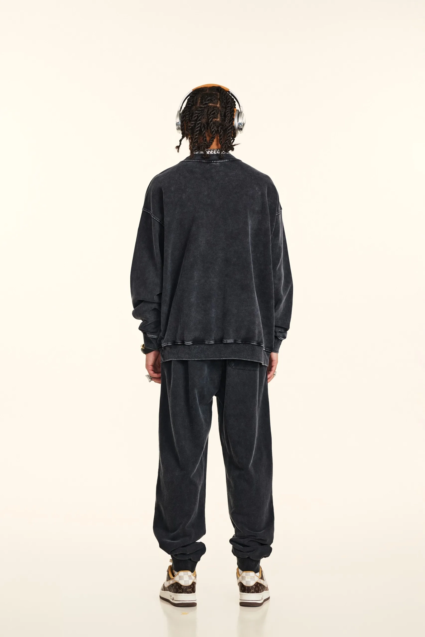 Person wearing a dark gray sweatshirt and pants with headphones on a white background