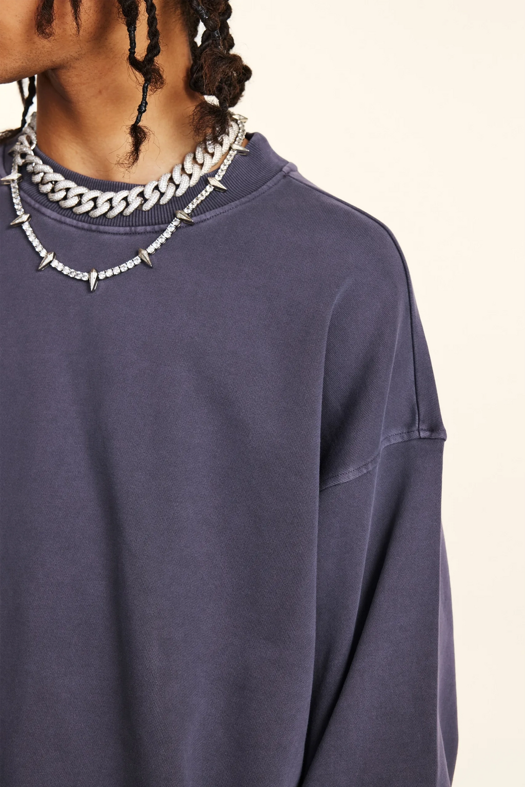Person wearing a dark blue sweatshirt with a necklace featuring spikes and chains.