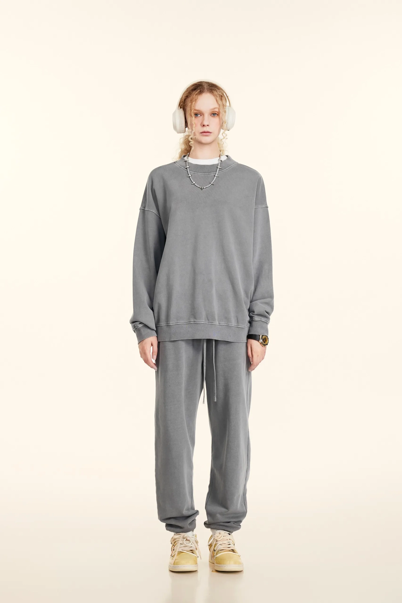 Person wearing a gray sweatshirt and pants with white headphones on a beige background