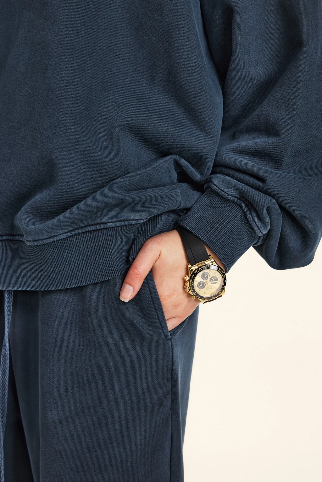 Person wearing a navy blue outfit with a gold watch on a beige background