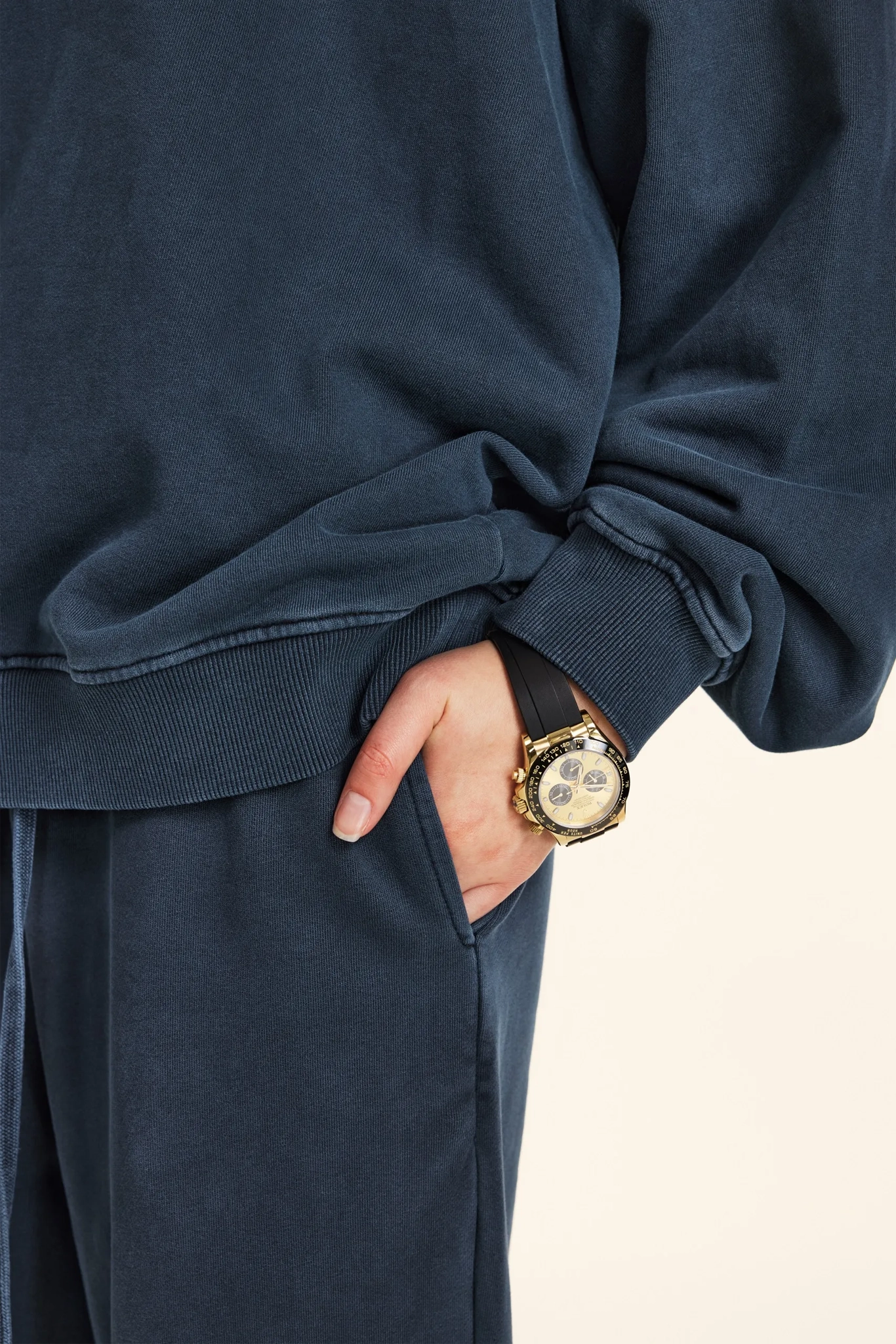 Person wearing a navy blue outfit with a gold watch on a beige background