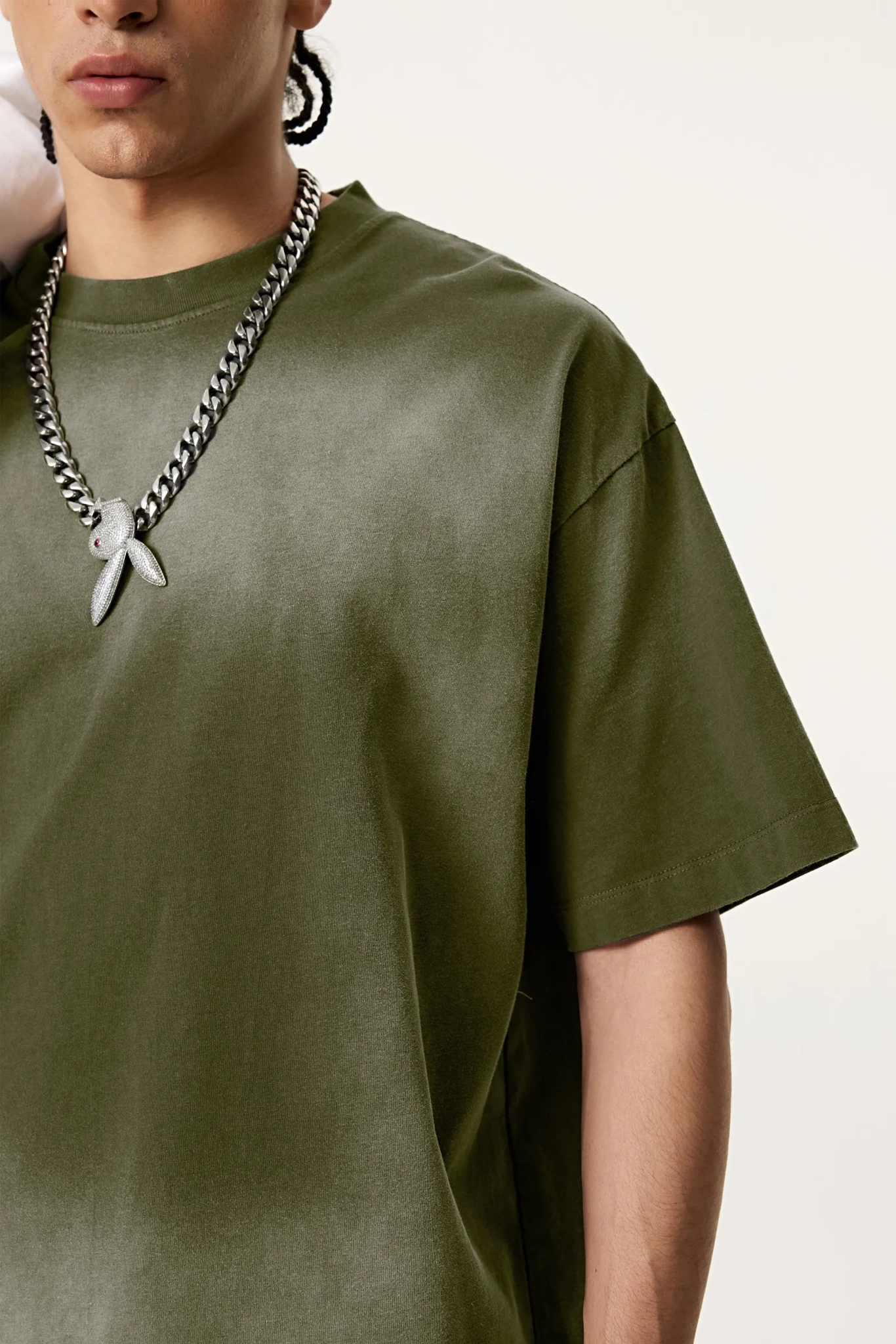 Person wearing an olive green t-shirt with a silver chain necklace on a white background