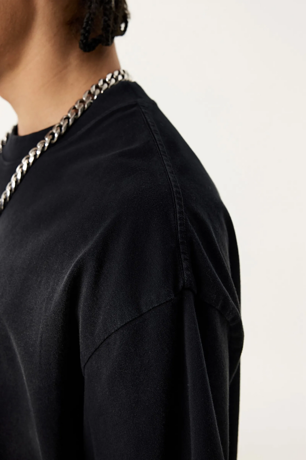 Person wearing a black shirt with a silver chain necklace on a white background