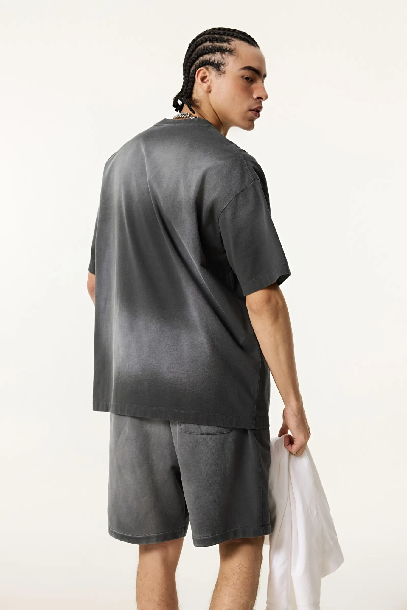 Person wearing a gray oversized t-shirt and shorts set on a white background