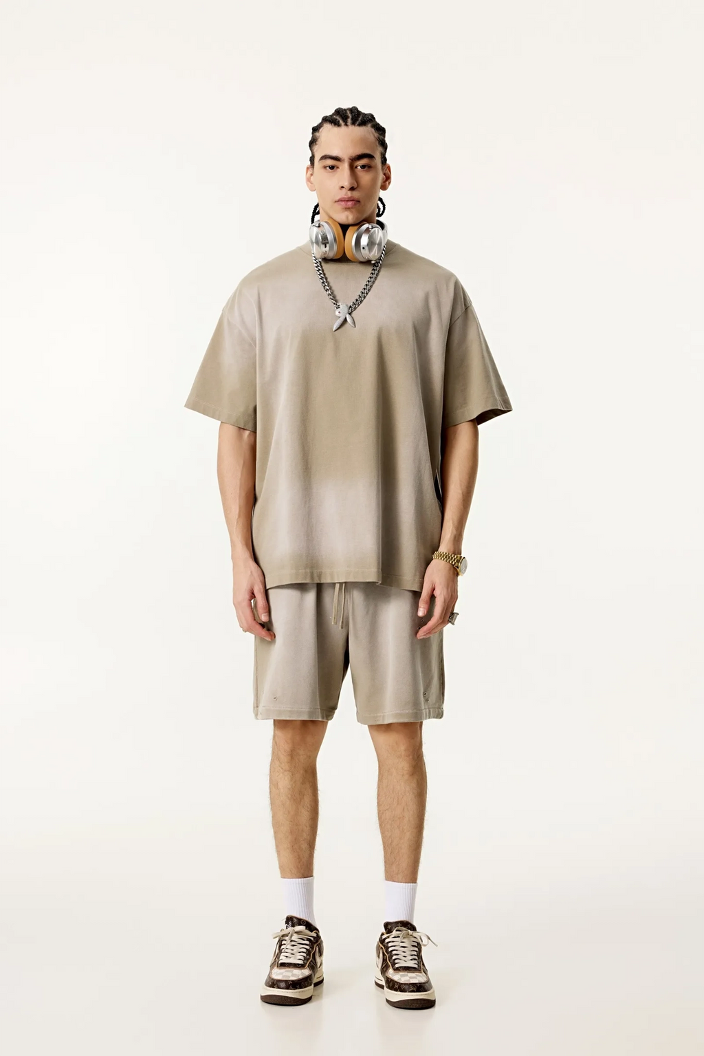 Person wearing a beige t-shirt and shorts set with sneakers on a white background