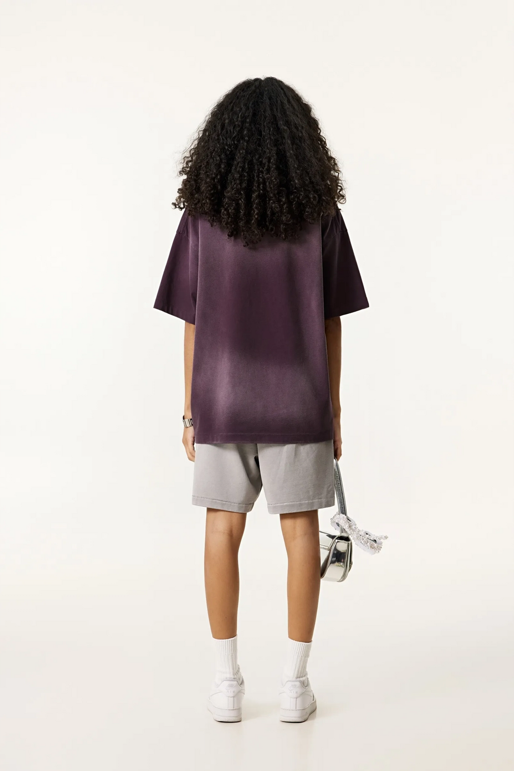 Person wearing a purple oversized t-shirt and gray shorts on a white background