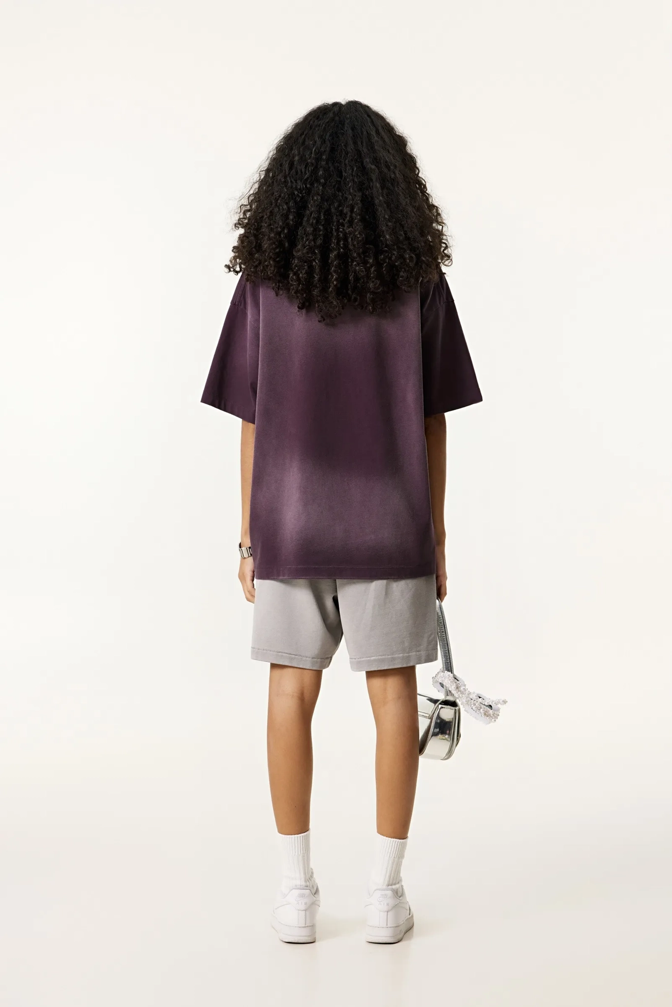 Person wearing a purple oversized t-shirt and gray shorts on a white background