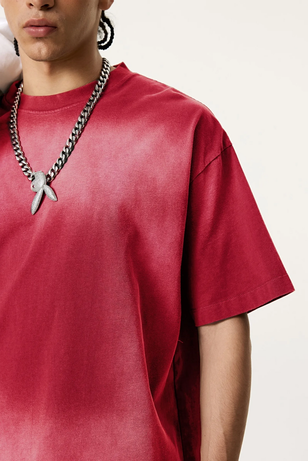 Person wearing a red t-shirt and a chain necklace with a pendant on a white background