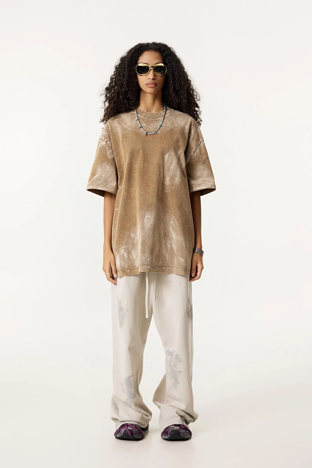 Woman wearing a beige top and white pants on a white background