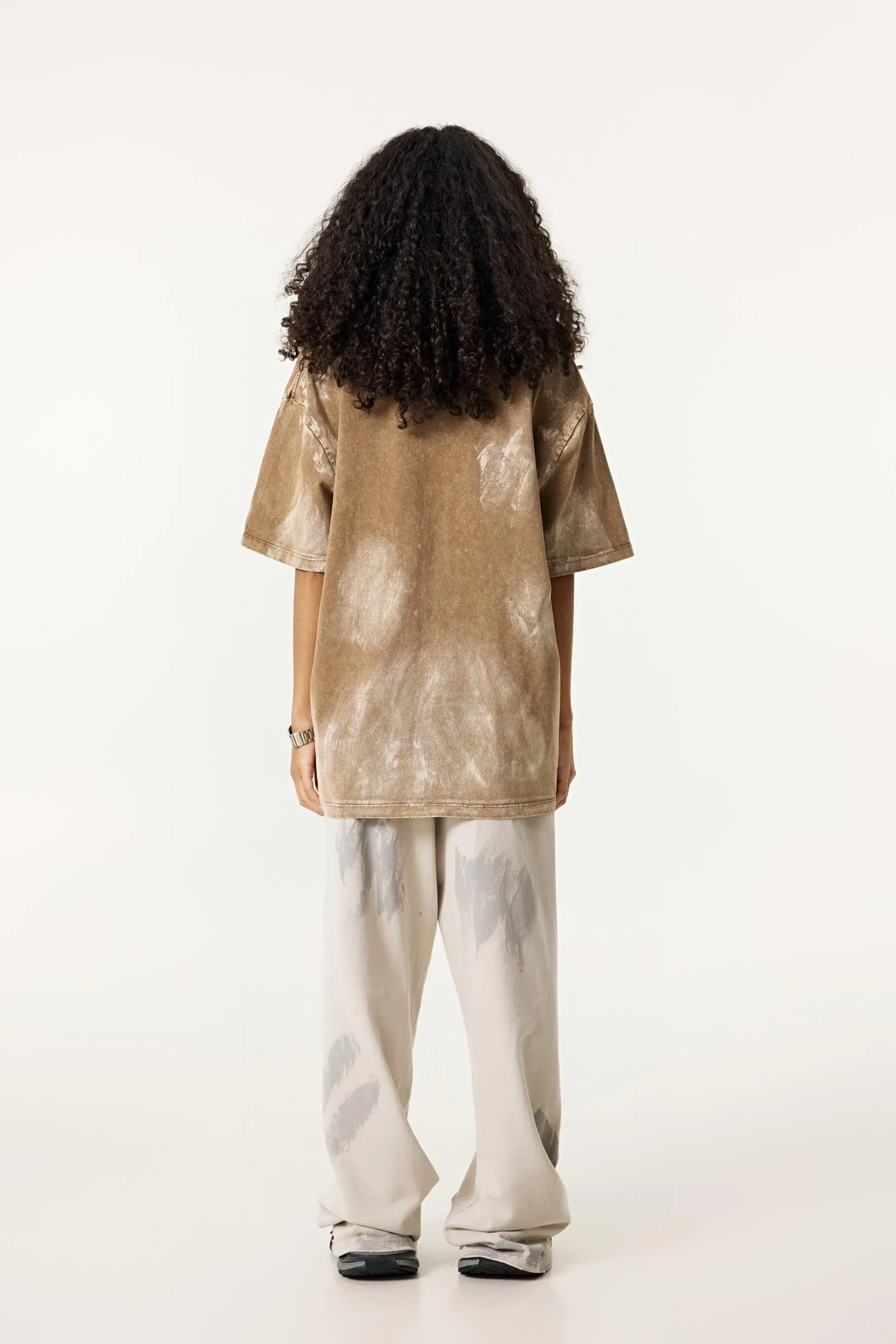 Person wearing a beige tie-dye shirt and light-colored pants on a white background