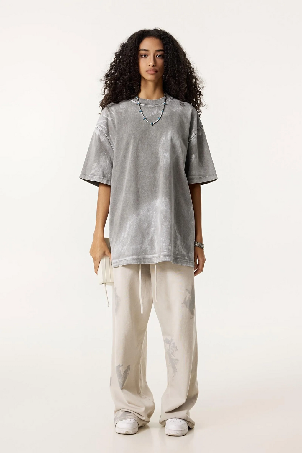 Person wearing a gray oversized t-shirt and white pants on a white background