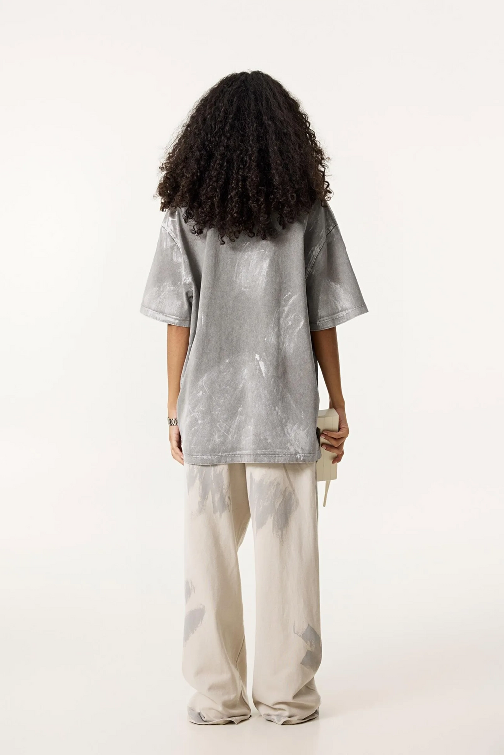 Person wearing a gray oversized t-shirt and light-colored pants on a white background