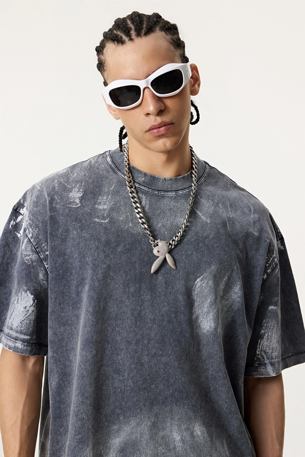 Person wearing a gray tie-dye t-shirt and white sunglasses on a plain background