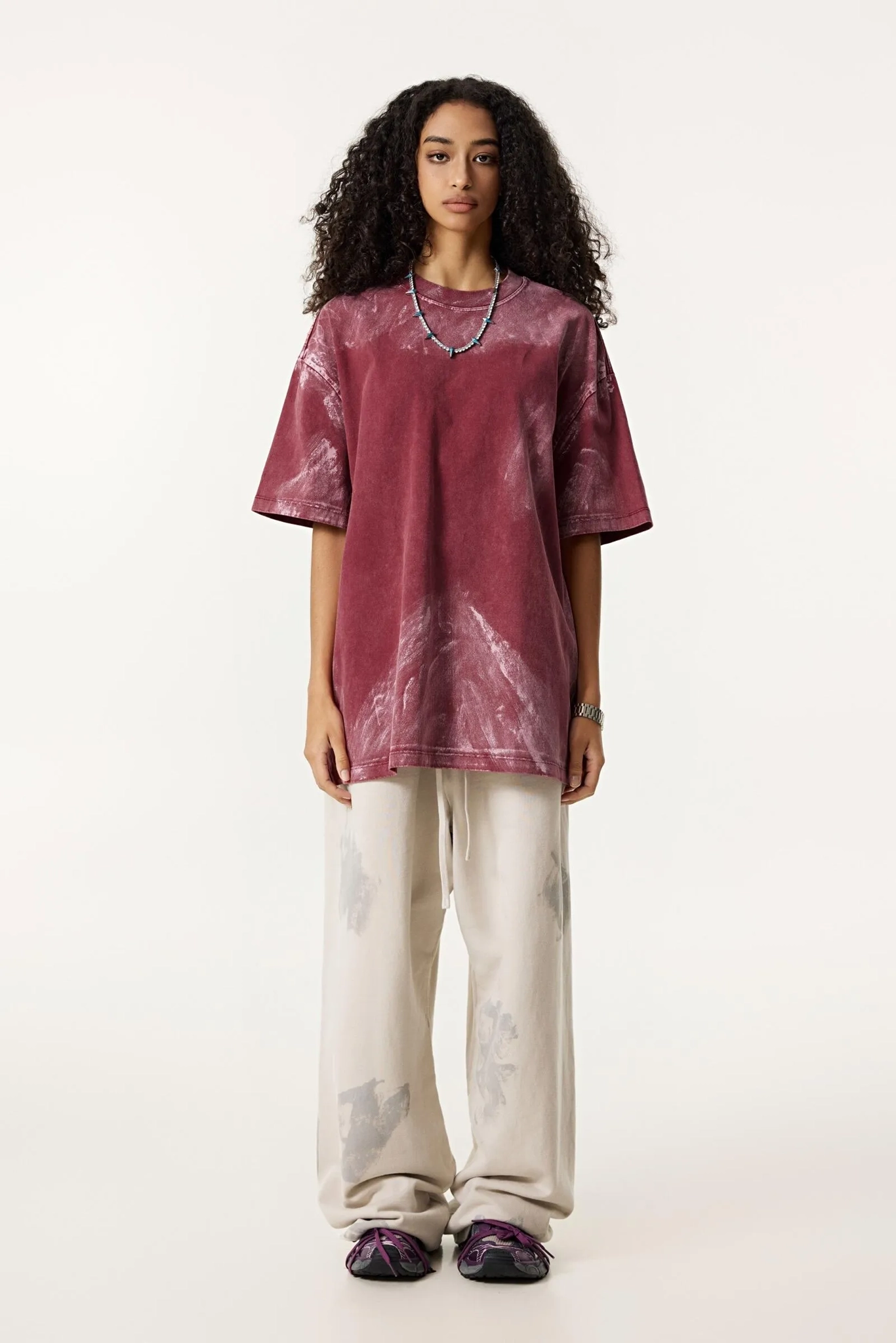 Woman wearing a maroon tunic and white pants on a white background