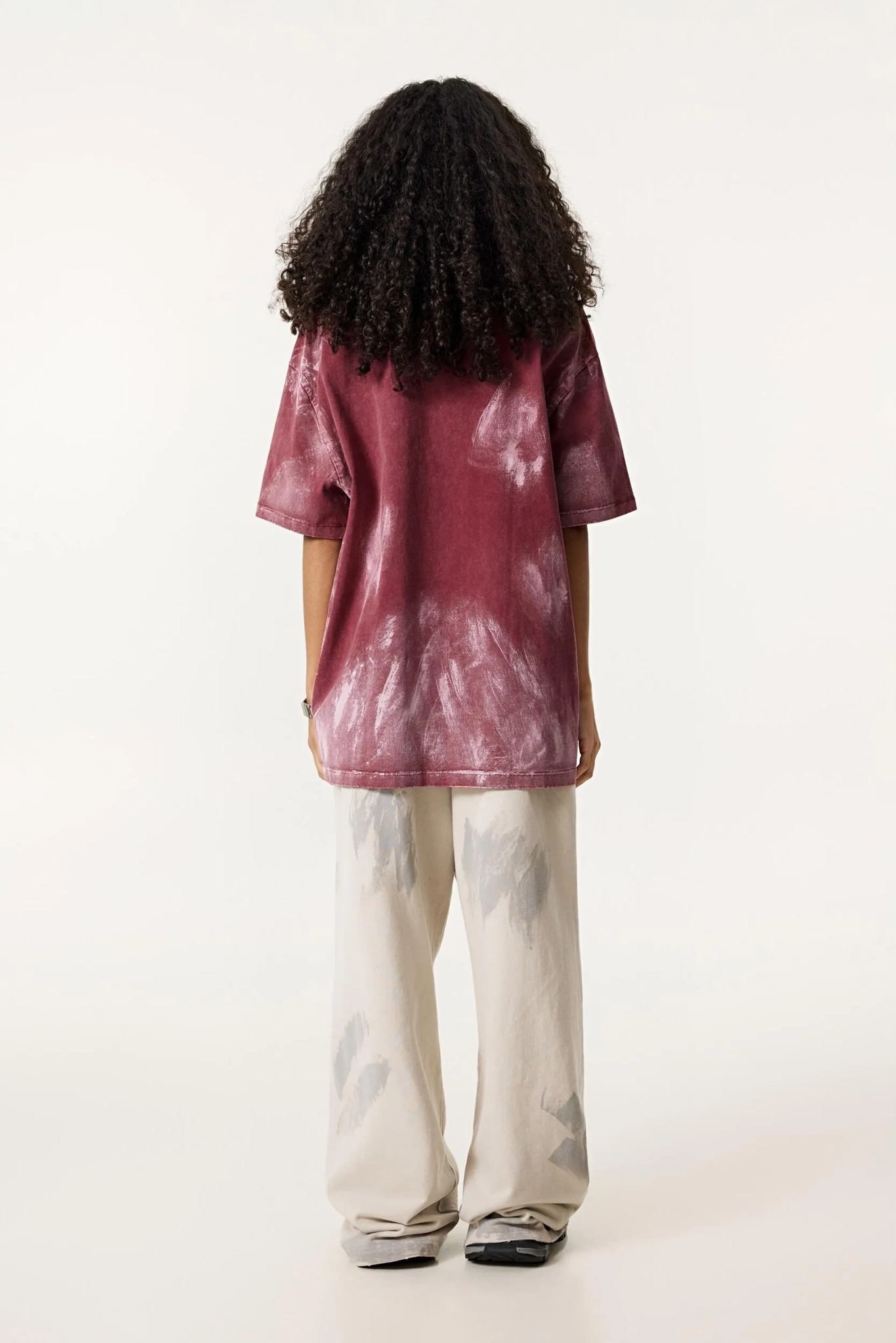 Person wearing a red tie-dye shirt and white pants on a white background