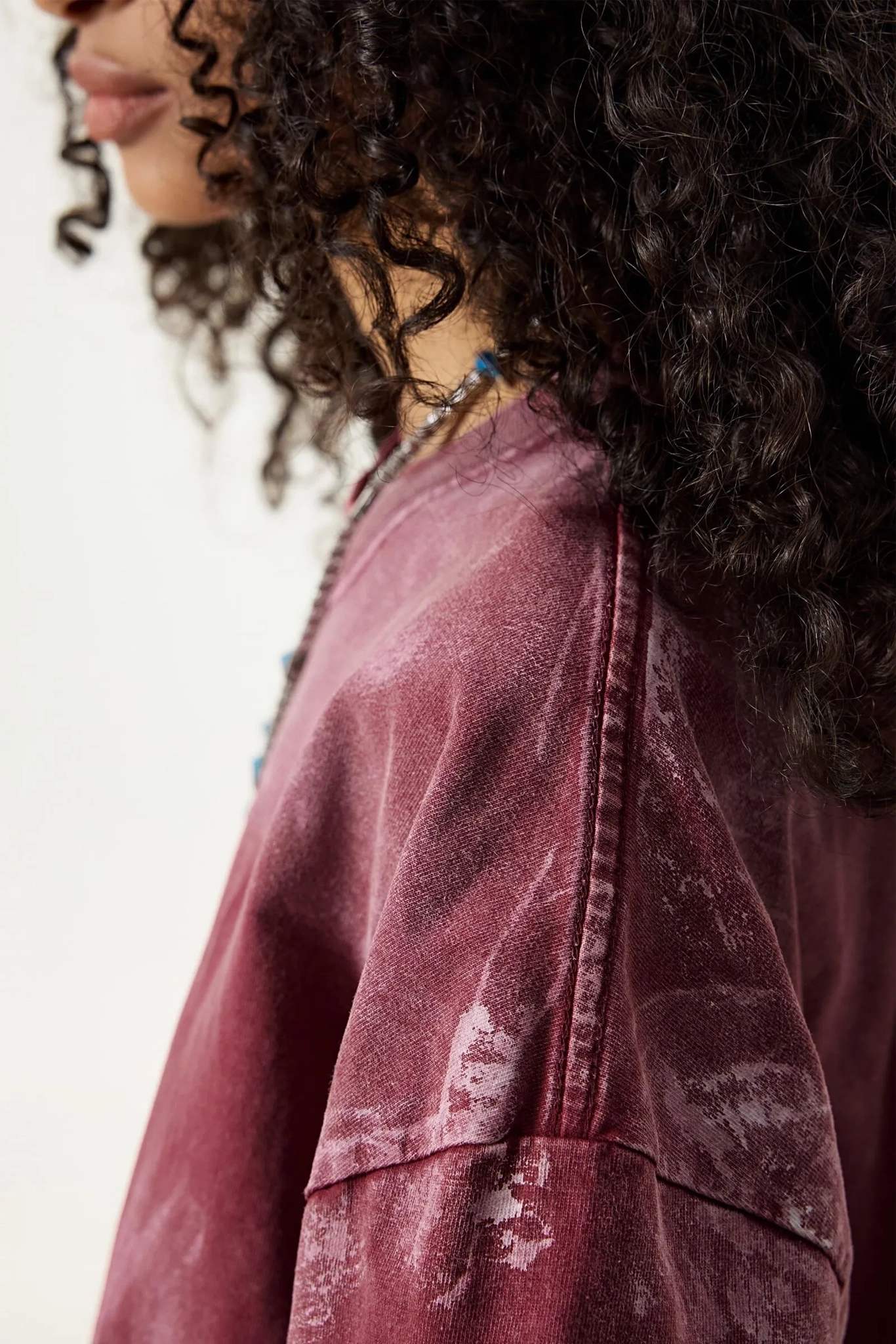 Close-up of a person wearing a maroon distressed denim jacket with a blurred background