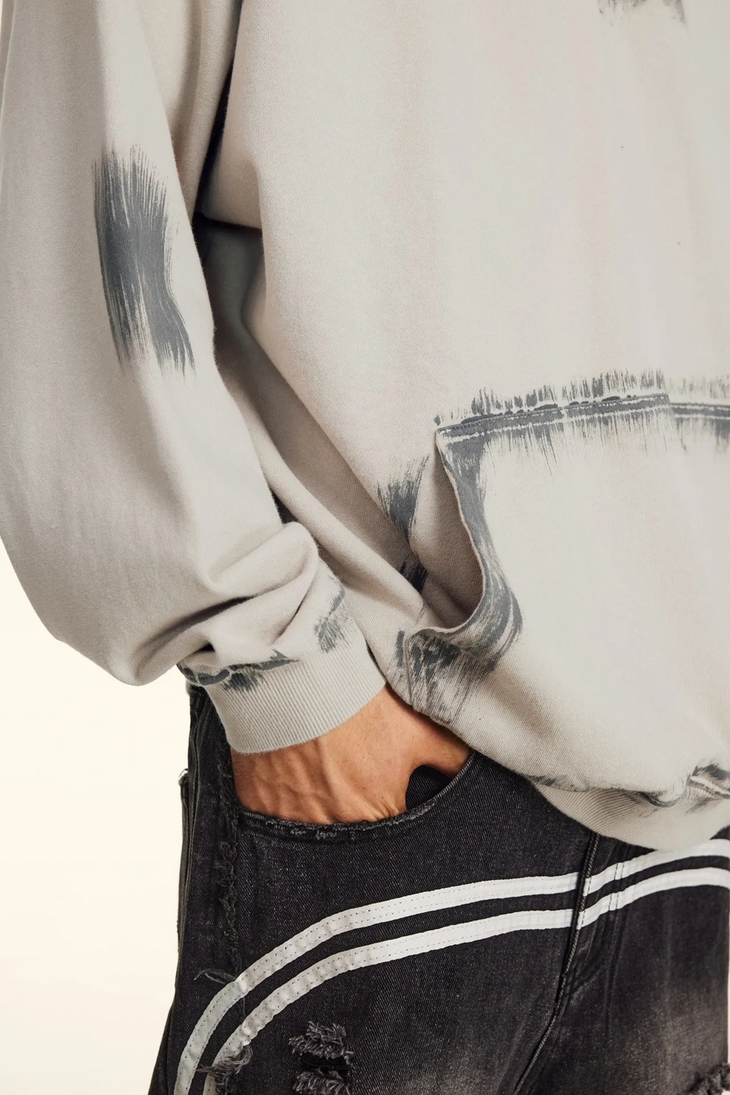 Close-up of a person wearing a light-colored sweatshirt with paint-like design and dark jeans.