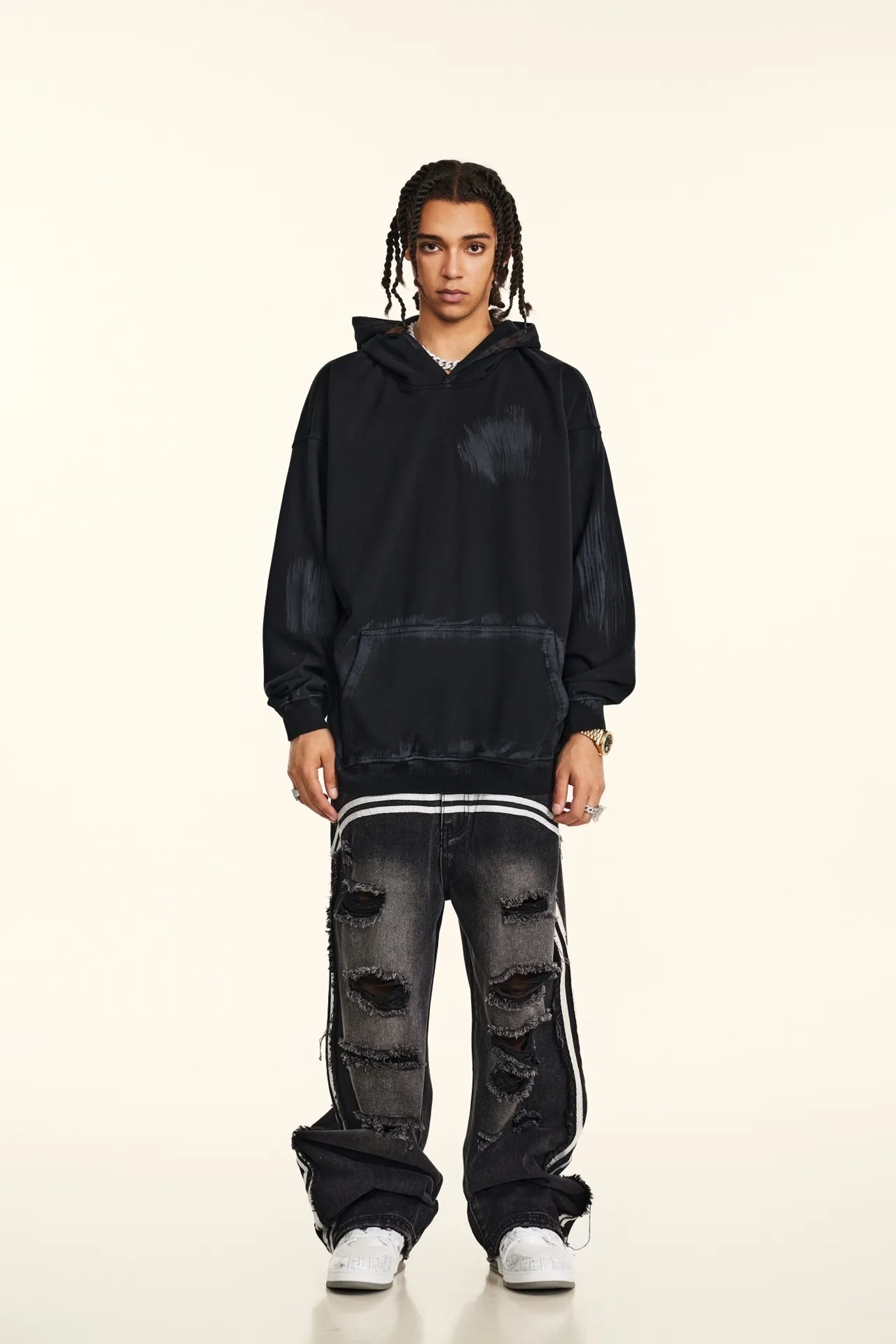 Person wearing a black hoodie and distressed jeans on a white background