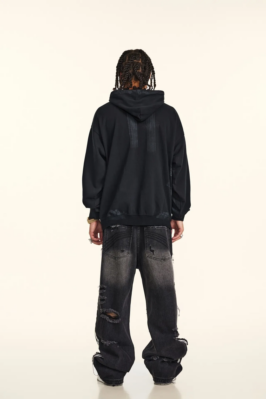 Person wearing a black hoodie and distressed jeans on a white background