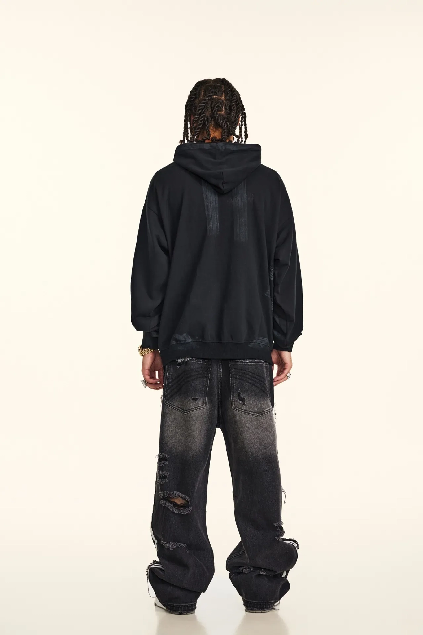 Person wearing a black hoodie and distressed jeans on a white background