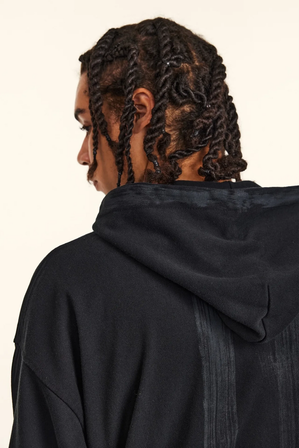 Person wearing a black hoodie with braided hair on a plain background