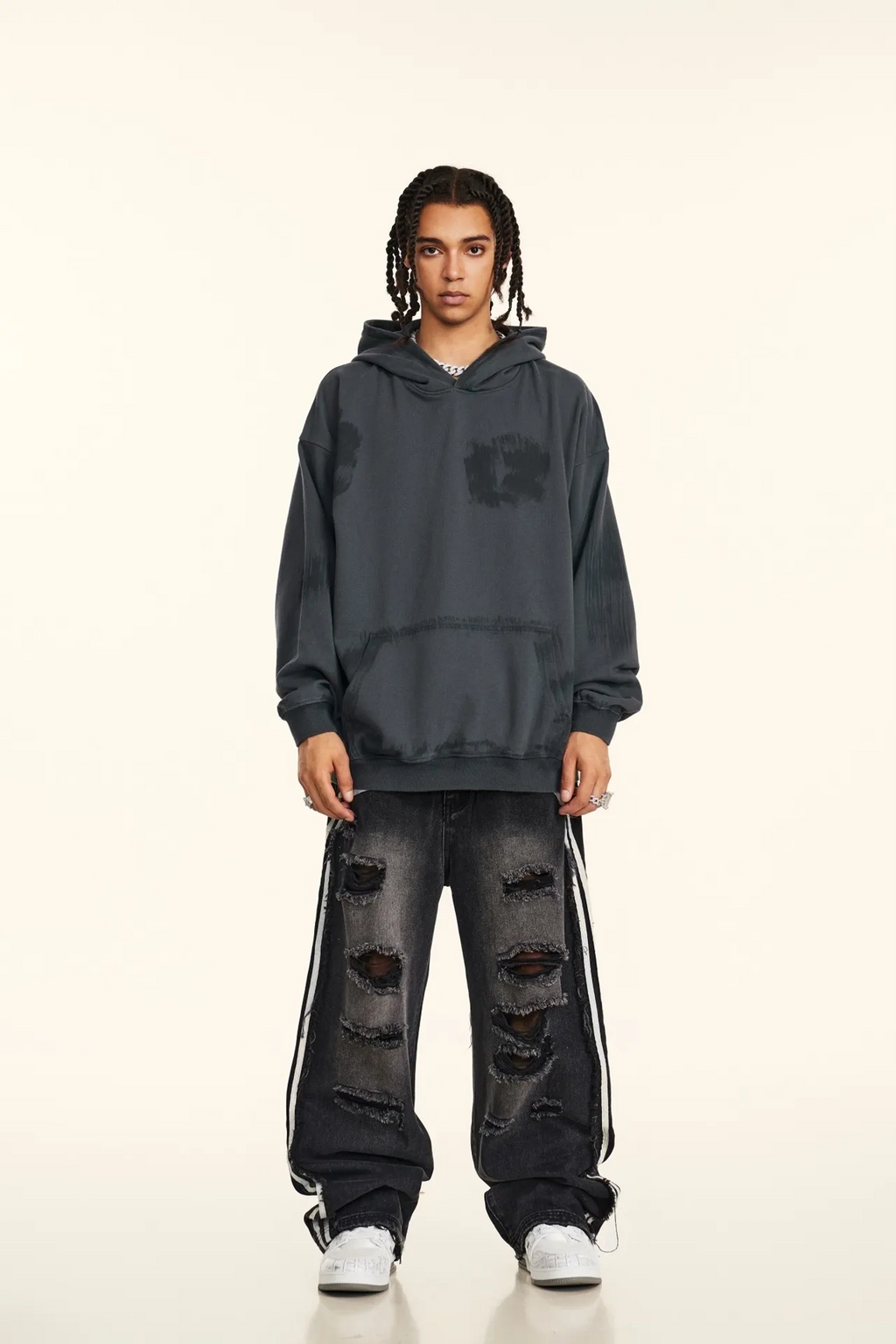 Person wearing a dark gray hoodie and distressed jeans on a white background